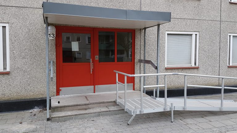 Röd entrédörr med glasfält och en ramp framför