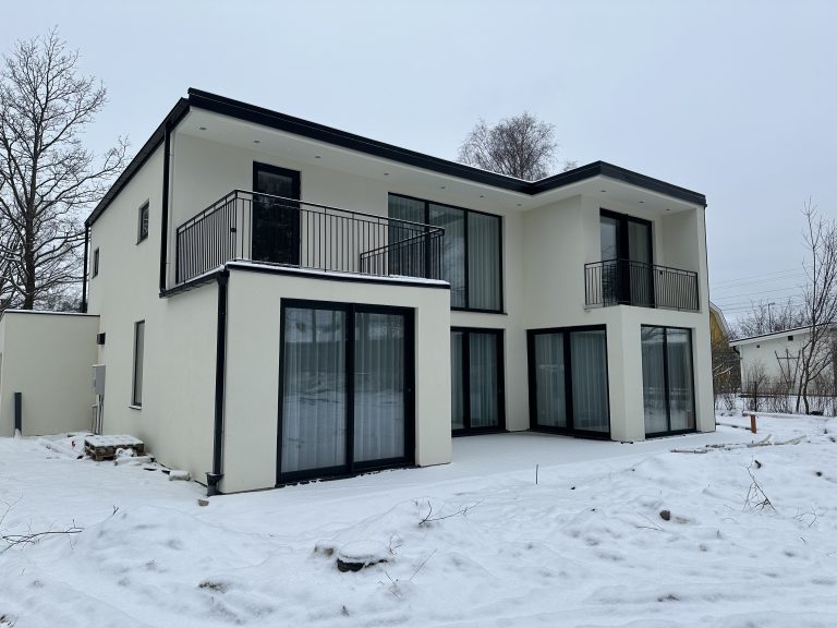 Vit villa med mörka fönster och glasdörrar i vintermiljö